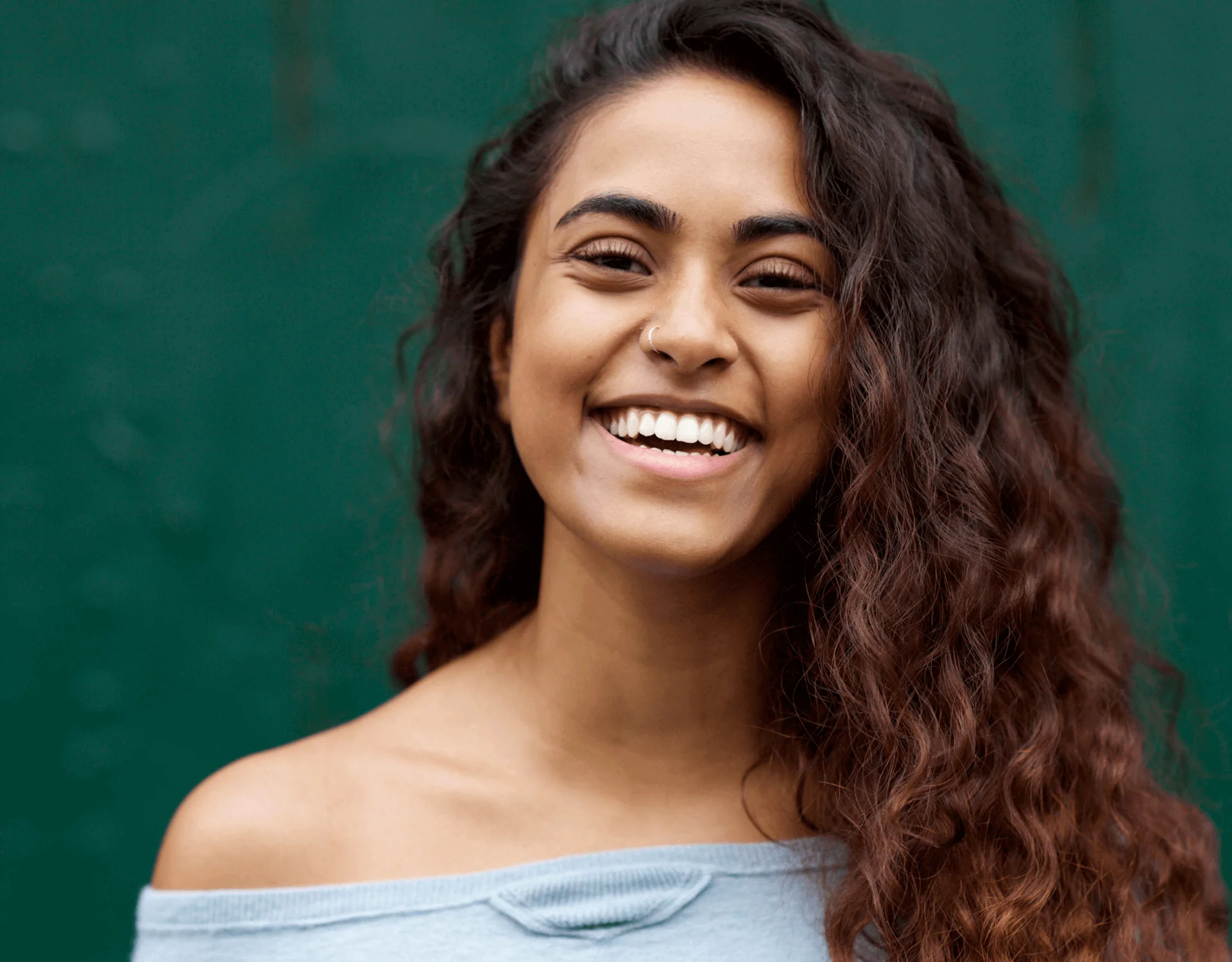 Smiling young woman with curly hair against a green background