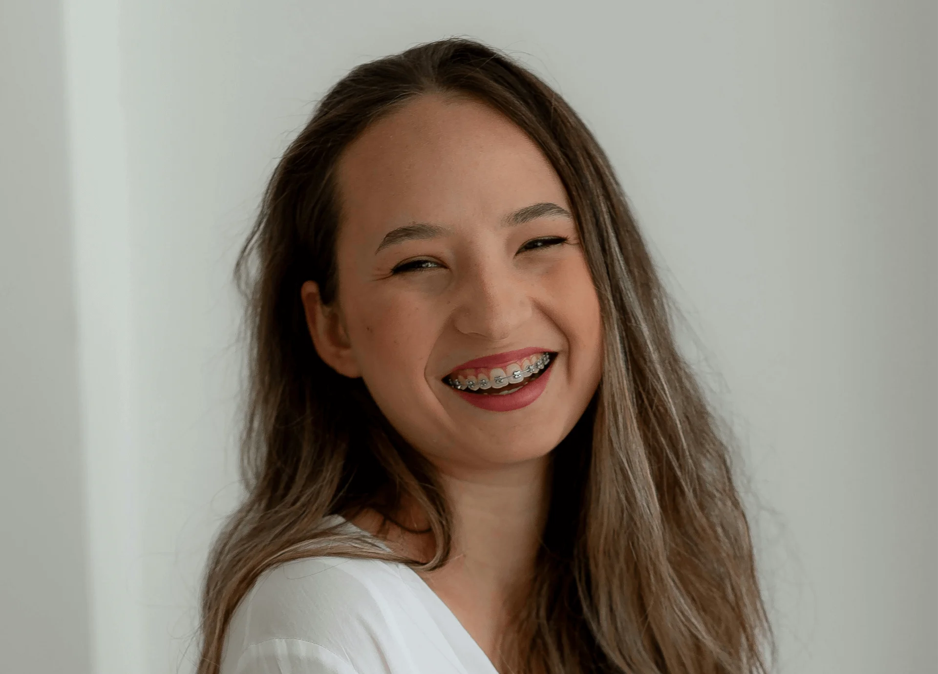 Smiling young woman with long brown hair showing metal braces on her teeth