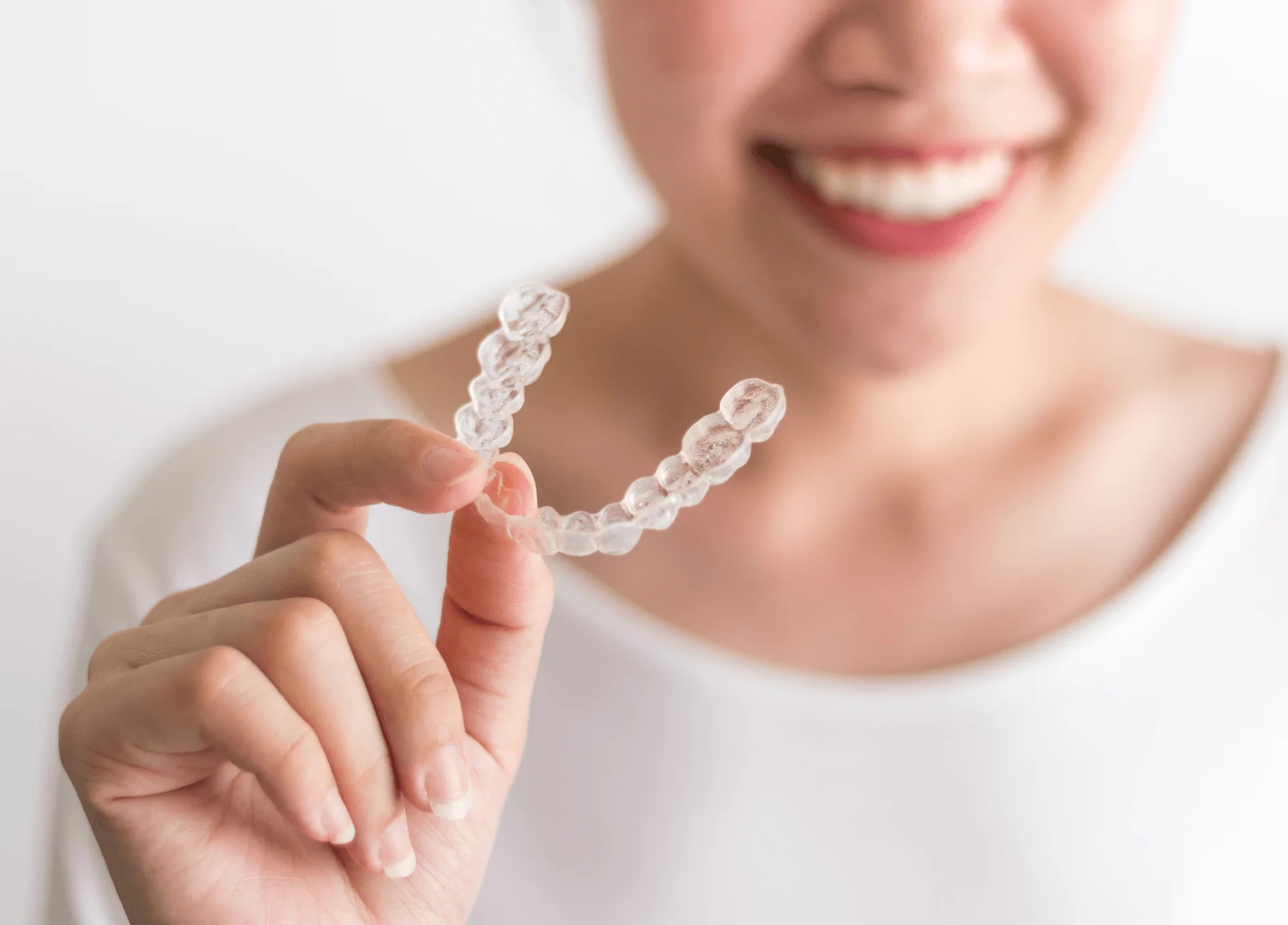 Smiling woman holding a clear plastic aligner tray between her fingers