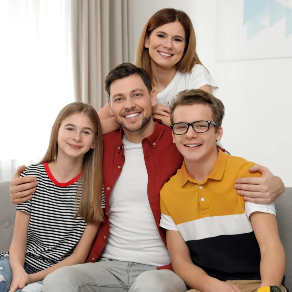 Smiling family of four posing together on a couch in a bright living room