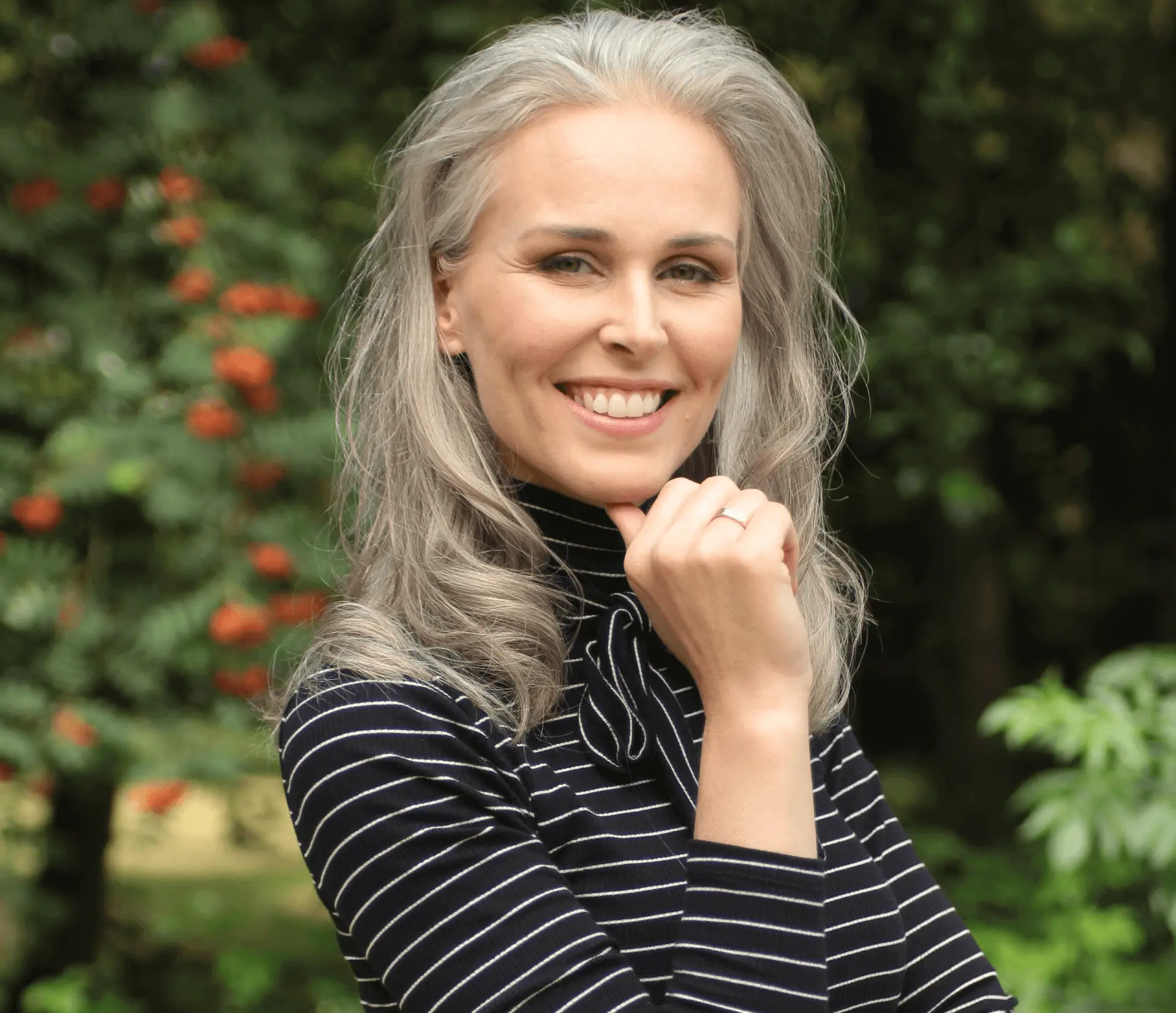 Smiling woman with long gray hair in a striped turtleneck outdoors