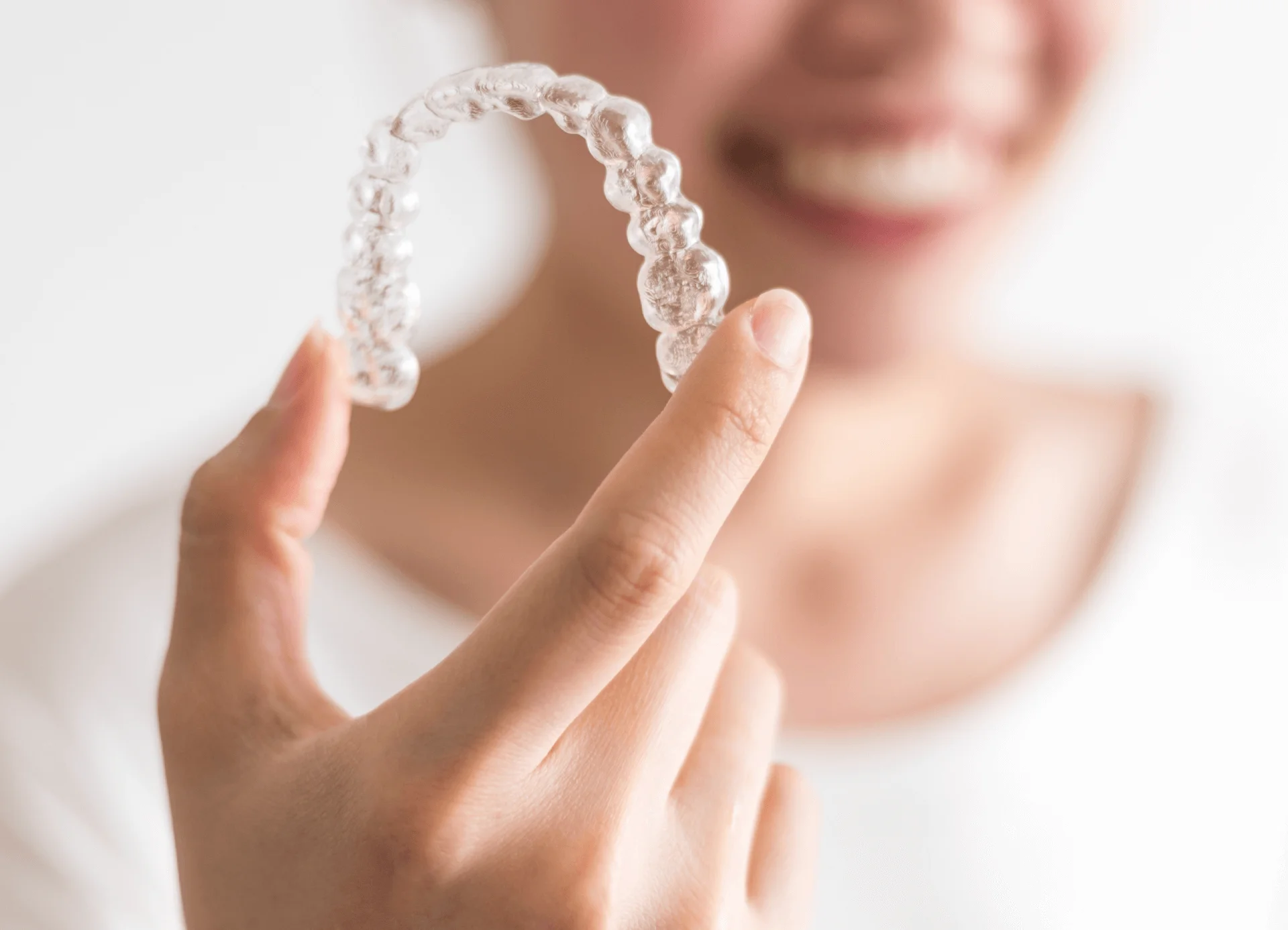 Smiling person holding a clear plastic aligner tray between fingertips