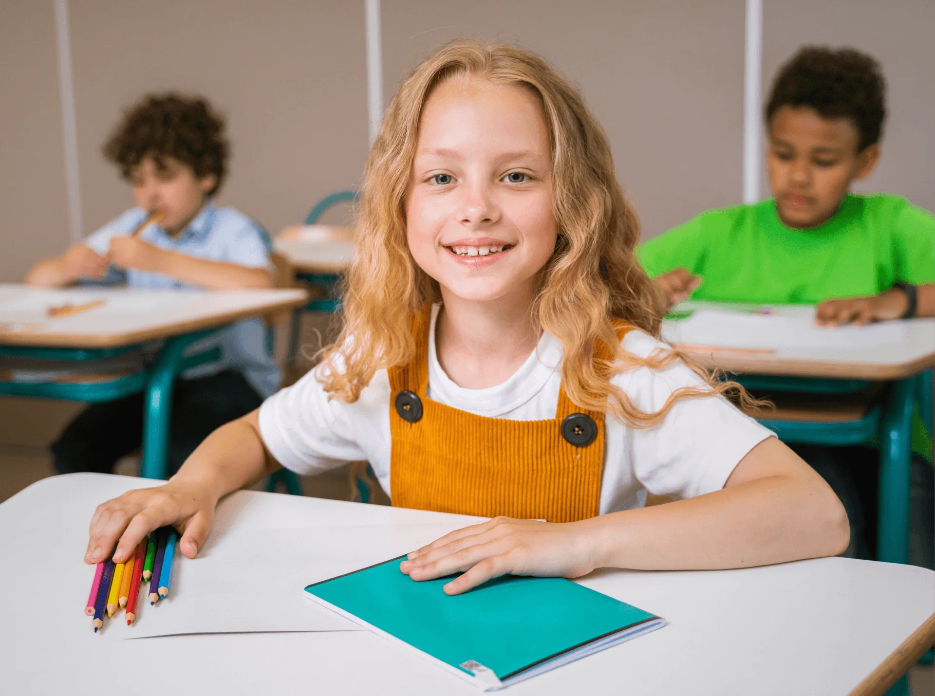 Smiling girl at a classroom desk with colored pencils and a notebook