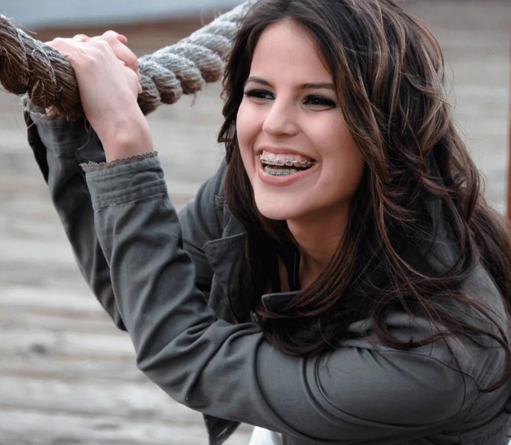 Smiling young woman with metal braces holding a thick rope, wearing a gray jacket