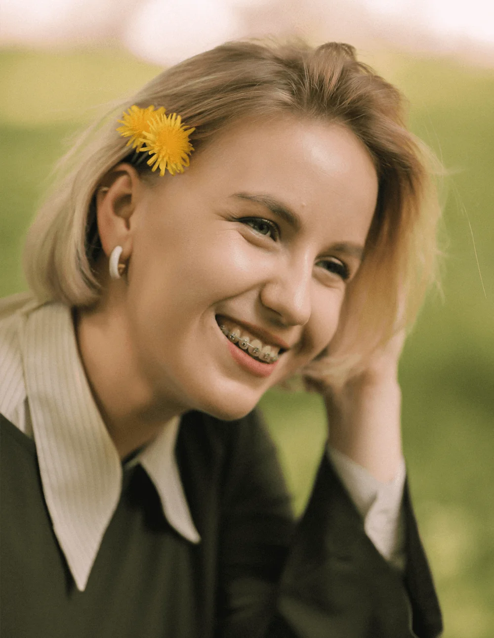 Smiling young woman with metal braces and yellow dandelions in her hair