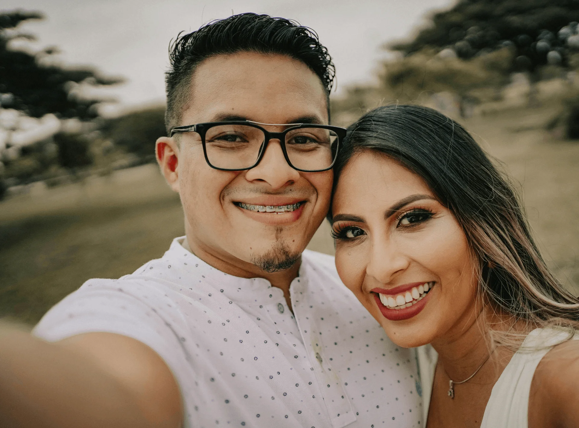 Smiling adult man with braces takes a selfie outdoors with a woman