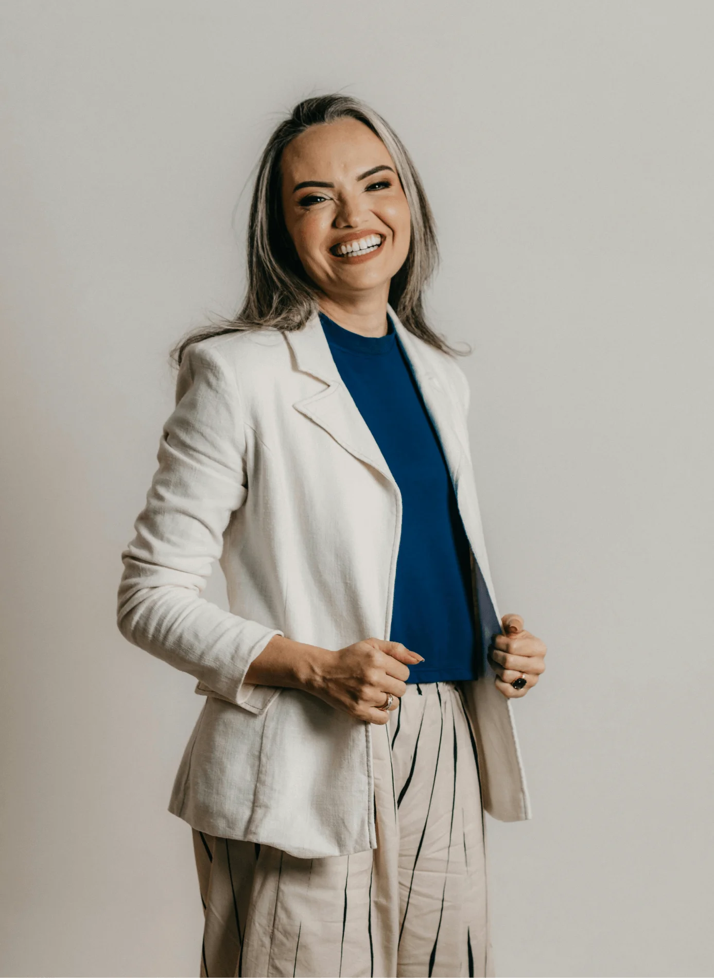 Smiling woman with gray hair in white blazer and blue top showing straight white teeth