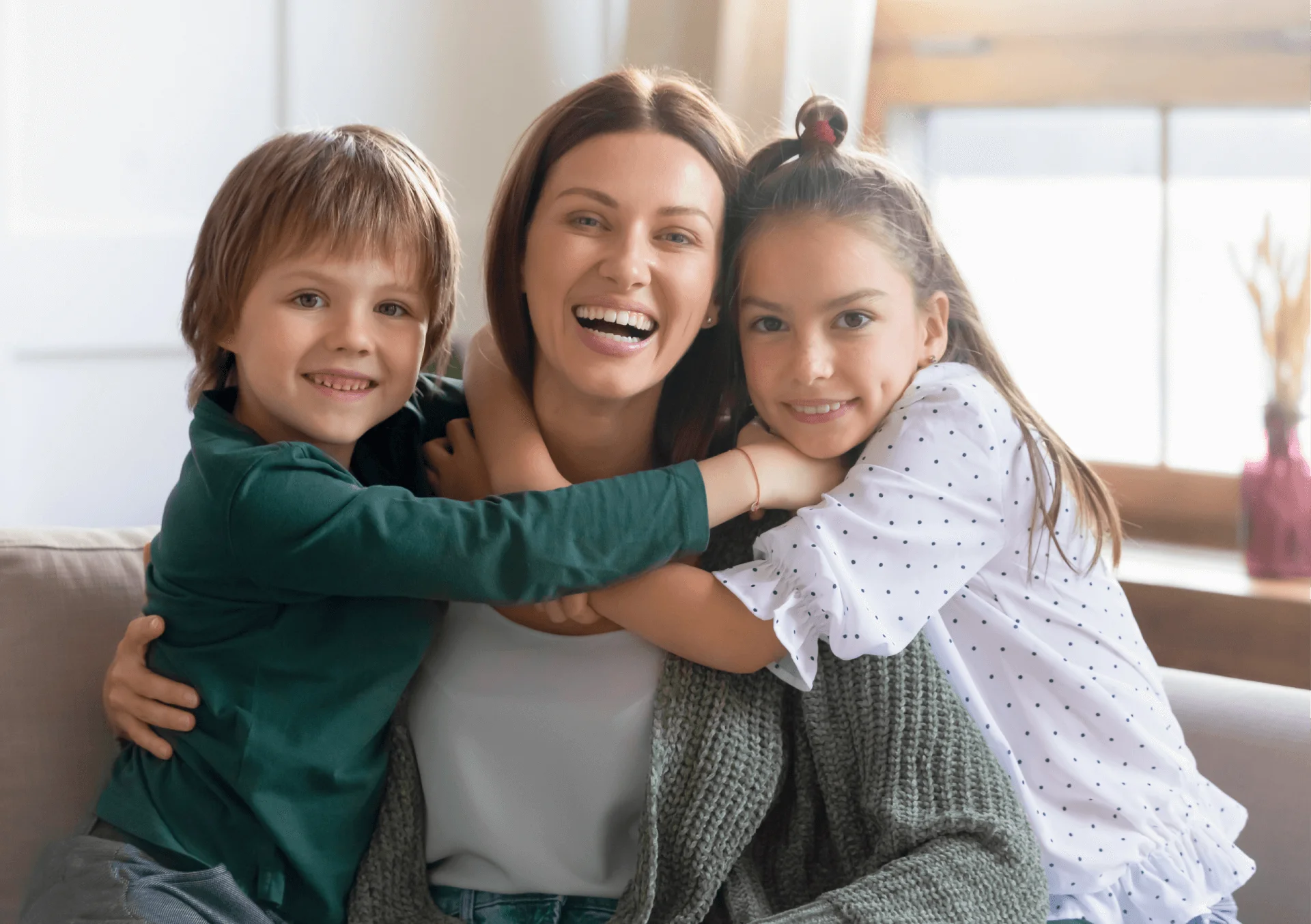 Smiling mother hugging her young son and daughter on a couch at home