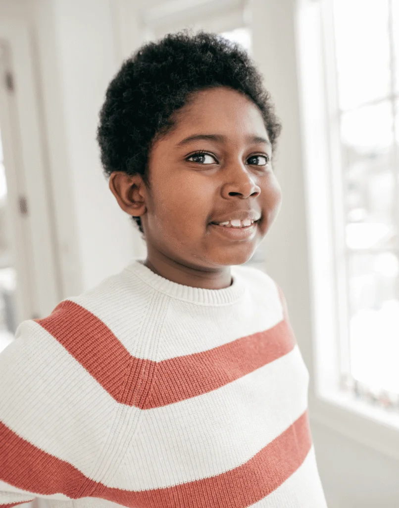 Smiling young boy in a striped sweater standing near a bright window