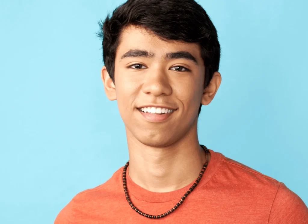 Smiling teen boy with straight white teeth on a light blue background
